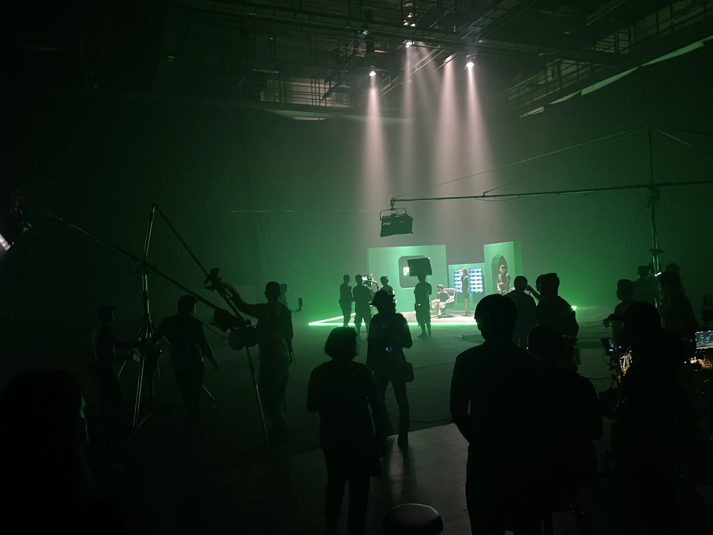 Crew and camera on a large sound stage with a built set under follow spots