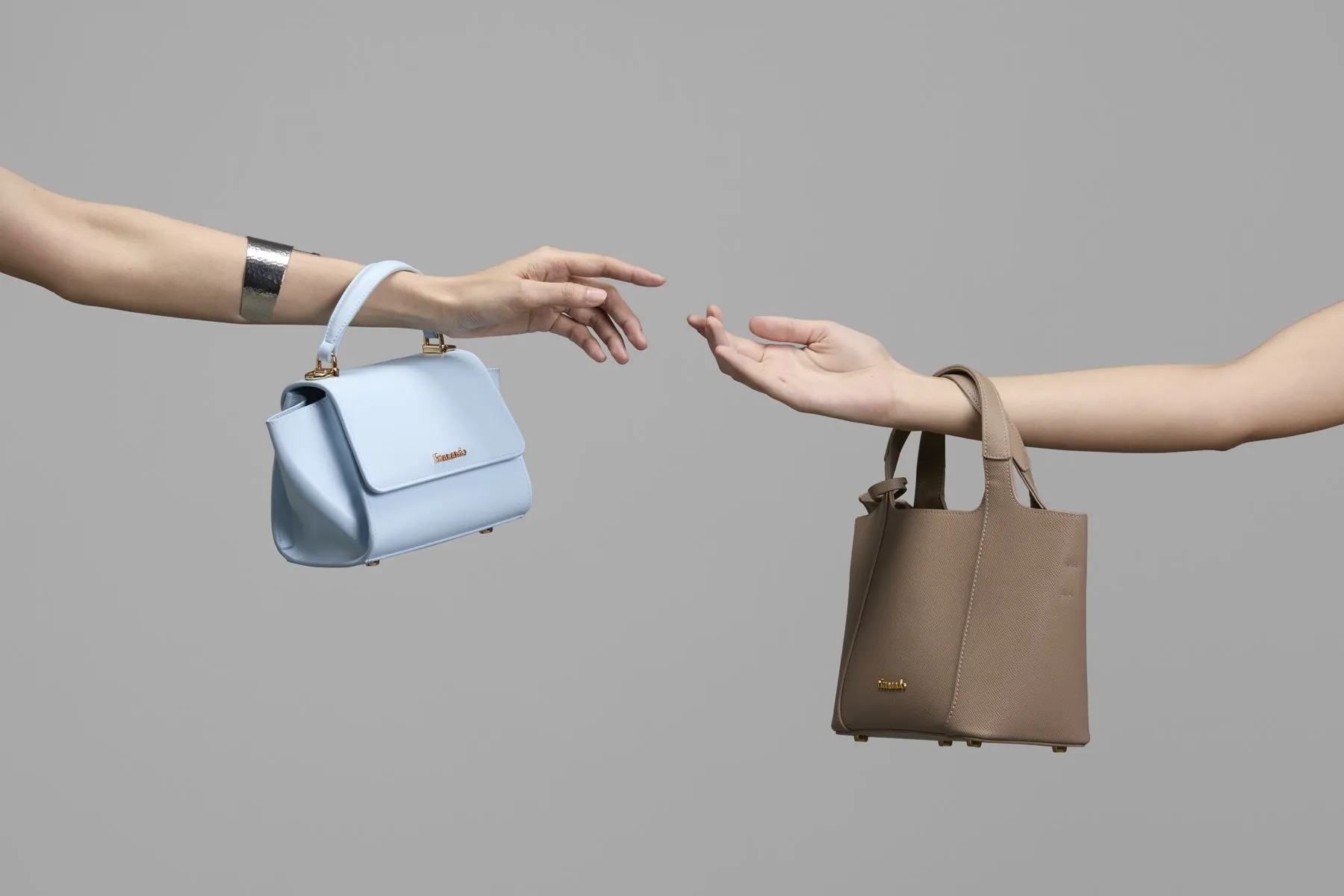 Two handbags held out on a grey studio set