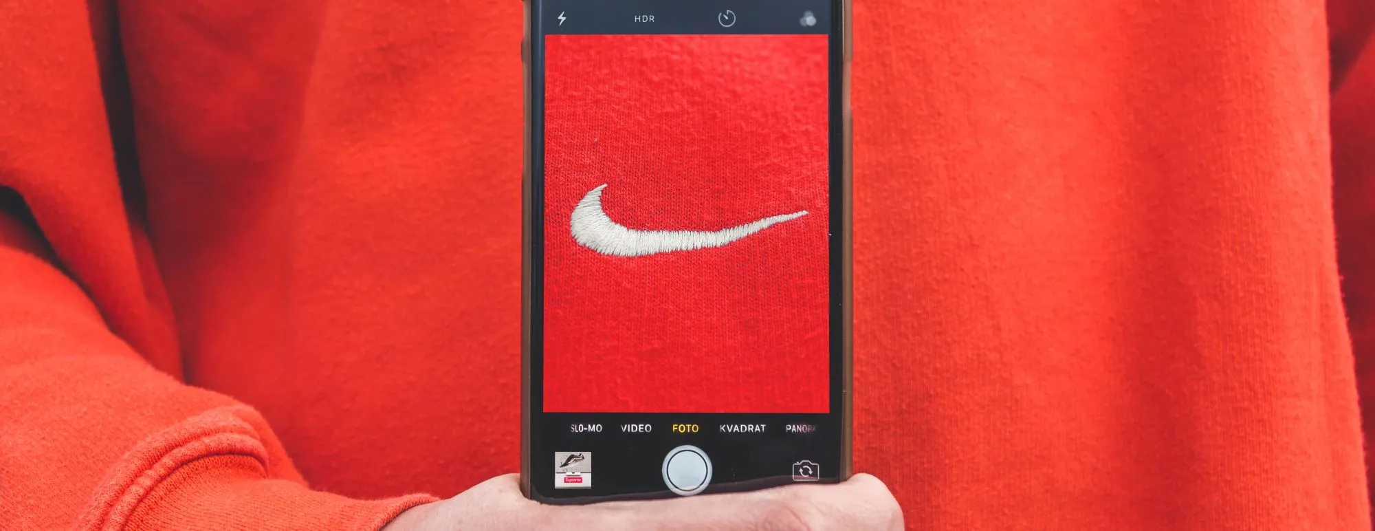 Hand holding a phone with a red brand screen against a red background