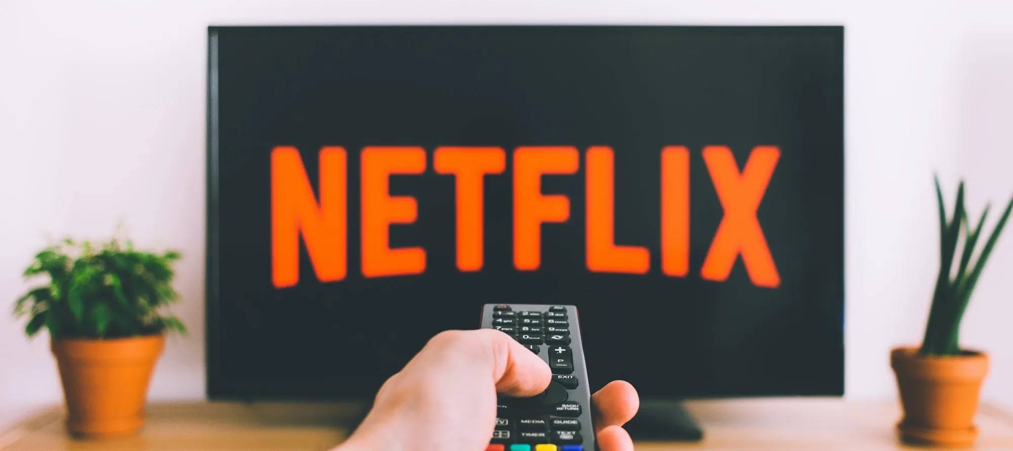 Hand pointing a remote control at a TV showing the Netflix logo