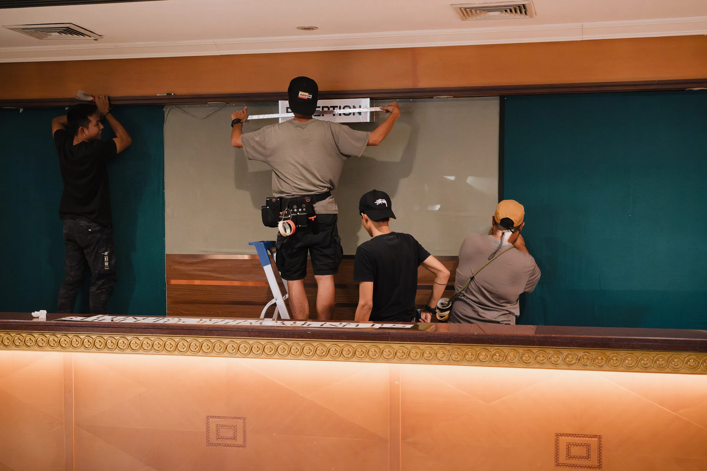 Art department crew fixing a sign to a dressed hotel wall for the KOKO music video