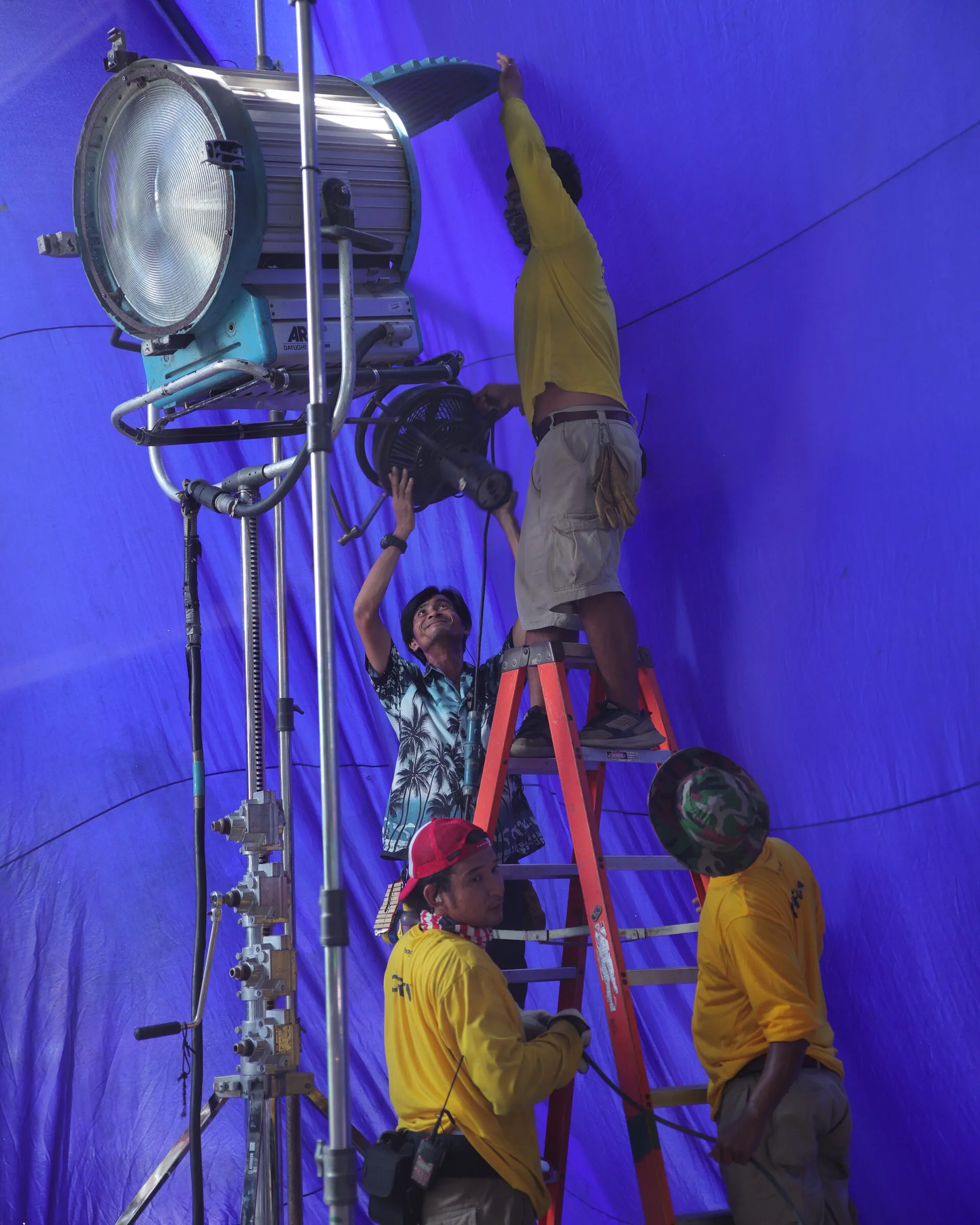 Lighting crew on a ladder rigging a large light against a purple studio cyc