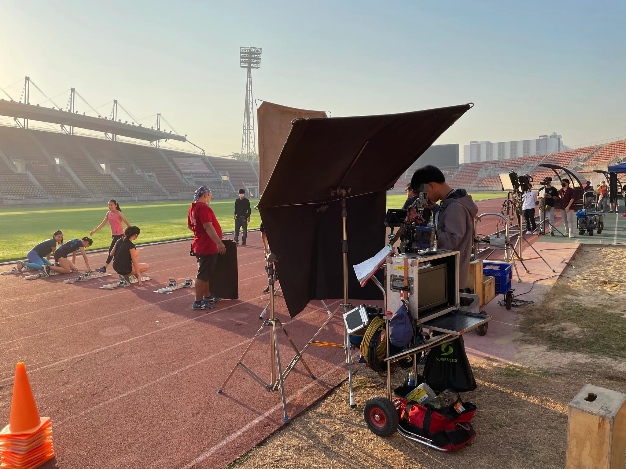 Crew setting up lights and a camera cart on a stadium running track